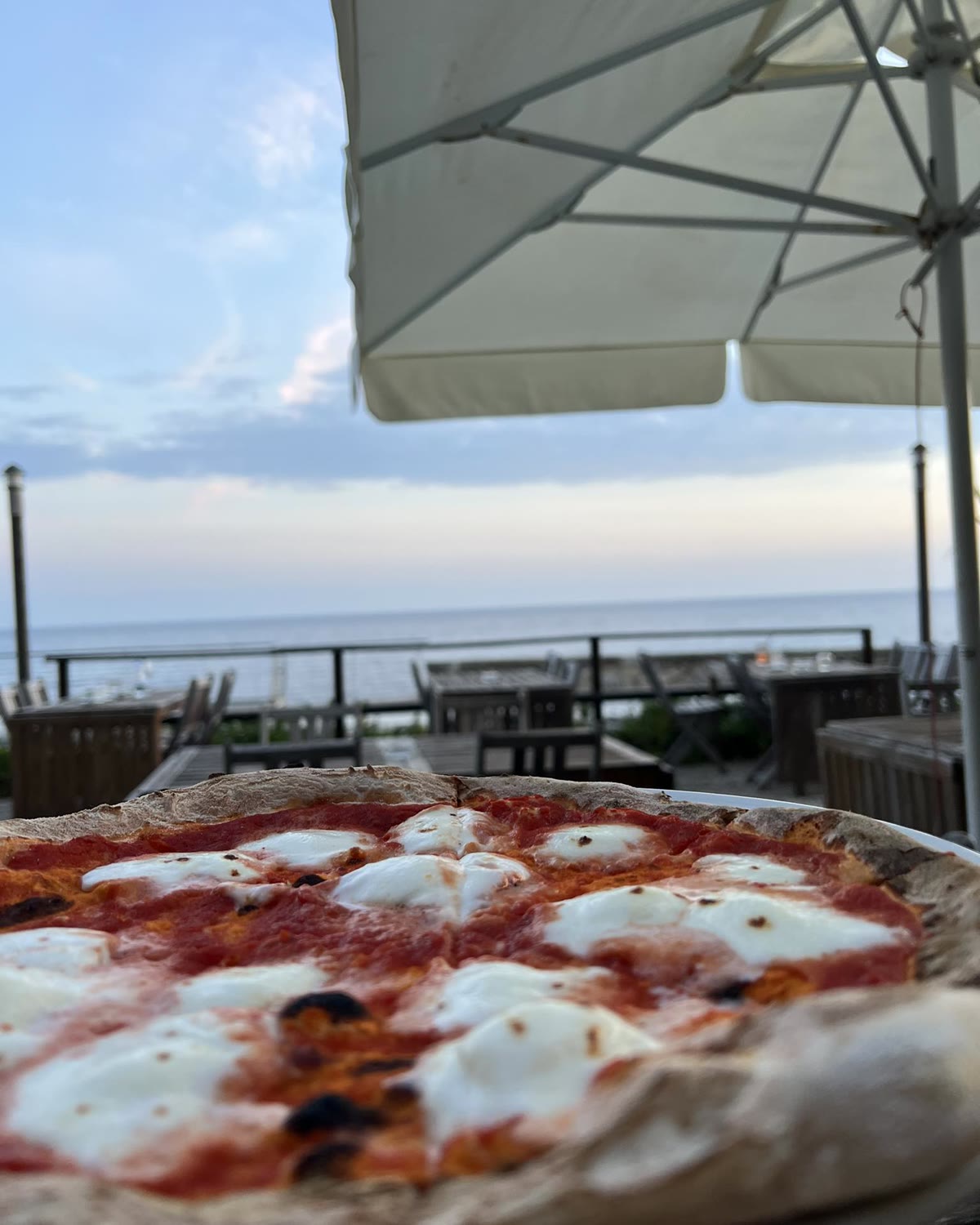 Pizza margherita servita in terrazza, sotto l'ombrellone, davanti al mare